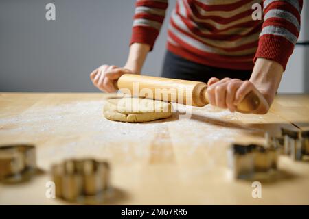 Unrecognizable woman rolls out ginger dough with rolling pin on kitchen table (selective focus photo) Stock Photo