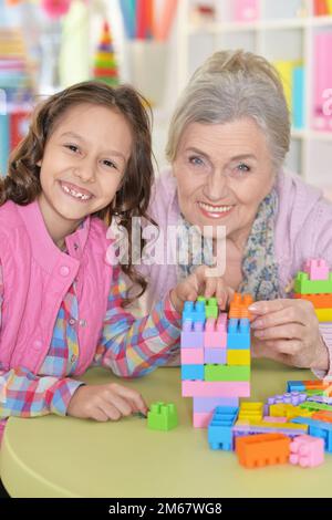 little girl and her grandmother playing with colorful plastic blocks Stock Photo