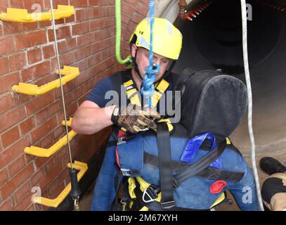 Firefighter Eddie Brant, 100th Civil Engineer Squadron Fire Department, fits an extraction harness onto a simulated victim during confined space training at Royal Air Force Mildenhall, England, April 14, 2022. The exercise scenario involved a teenager (simulated by the mannequin) who fell and was injured after climbing down into an underground facility. Another firefighter simulated also falling after slipping on a broken step while climbing down to rescue the victim, so other firefighters from his team had to complete the rescue. Stock Photo