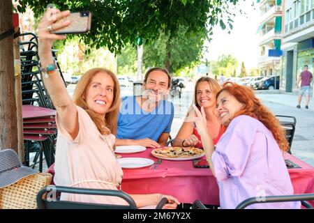 Mature friends making selfie photo while sitting on a restaurant terrace. Stock Photo