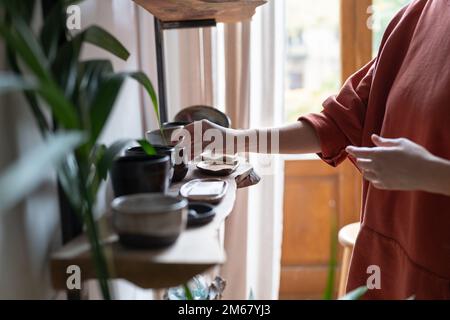 Pottery business owner arranging handmade ceramic products on shelf  Stock Photo