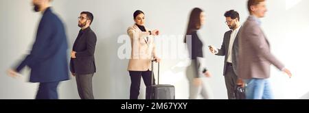 Motion blurred people walking near business woman who is looking at wristwatch in hurry to flight. Stock Photo