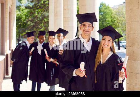 Happy couple students in graduation dresses and hats enjoy graduation ceremony together. Stock Photo