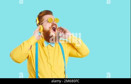 Funny stylish fat man in headphones listens to music and sings loudly on light blue background. Stock Photo