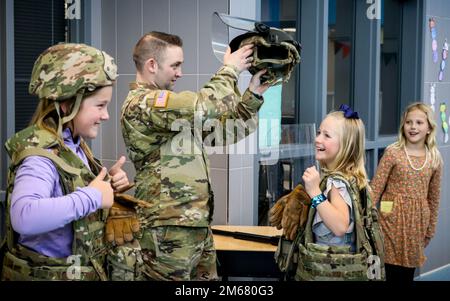 Capt. Nathan Hoeger, commander of the 186th Military Police Company, Iowa Army National Guard, puts a vest and helmet on a student at Heritage Elementary School during a STEM+Art event in Ankeny, Iowa, on April 14, 2022. Hoeger and other members of the 186th MP Company showed how science, technology, engineering and math are used in the Iowa National Guard to protect Soldiers and complete missions through interactive displays. Stock Photo