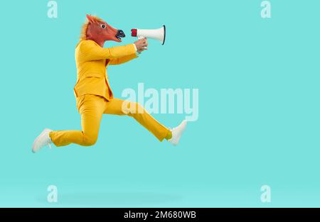 Man in horse head mask jumping and shouting in megaphone Stock Photo