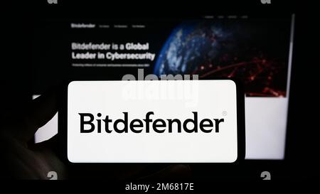 Person holding smartphone with logo of Romanian cybersecurity company Bitdefender on screen in front of website. Focus on phone display. Stock Photo