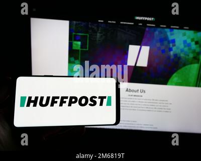 Person holding smartphone with logo of US news company HuffPost on screen in front of website. Focus on phone display. Stock Photo