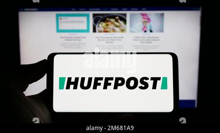 Person holding cellphone with logo of US news company HuffPost on screen in front of business webpage. Focus on phone display. Stock Photo