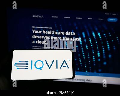 Person holding smartphone with logo of US health technology company IQVIA Holdings Inc. on screen in front of website. Focus on phone display. Stock Photo