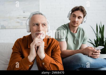 pensive and positive man listening music in wireless headphones near young son with smartphone,stock image Stock Photo