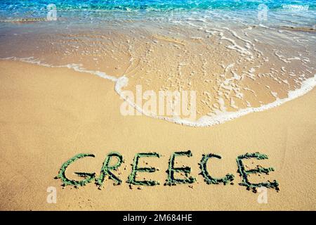 Inscription GREECE on a sandy beach with sea waves. Nature background Stock Photo