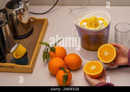 woman's hands squeezing oranges in a juicer in her kitchen at home Stock Photo