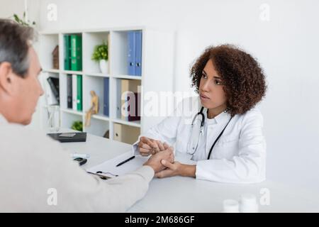 African american doctor checking hand of patient with diabetes and talking in clinic,stock image Stock Photo