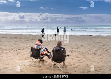 Two holidaymakers sitting on folding chairs on Fistral Beach looking out to sea in Newquay in Cornwall in England in the UK. Stock Photo