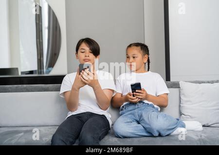 Asian kids using smartphones and sitting on couch at home,stock image Stock Photo