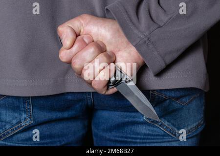 Criminal with knife weapon hidden behind his back. Stock Photo