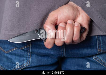 Criminal with knife weapon hidden behind his back. Stock Photo