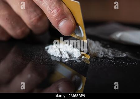 Man use credit card to make cocaine drug powder lines on black table. Stock Photo