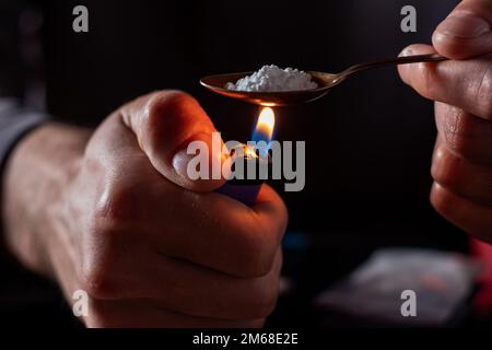 Drug addicts in the dark room. Addict preparing drugs with a spoon and lighter. White powder and a syringe. Drug concept. International drug abuse day Stock Photo