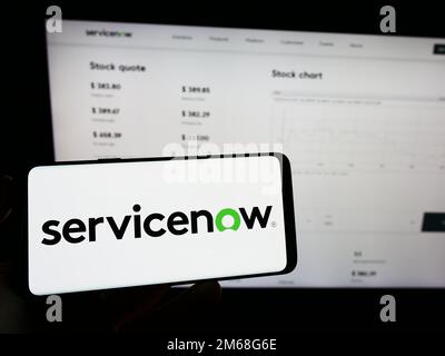 Person holding mobile phone with logo of American software company ServiceNow Inc. on screen in front of web page. Focus on phone display. Stock Photo