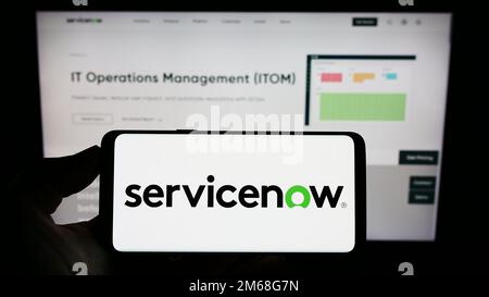 Person holding smartphone with logo of US software company ServiceNow Inc. on screen in front of website. Focus on phone display. Stock Photo
