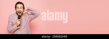 Amazed host of event holding microphone and looking at camera isolated on pink, banner,stock image Stock Photo