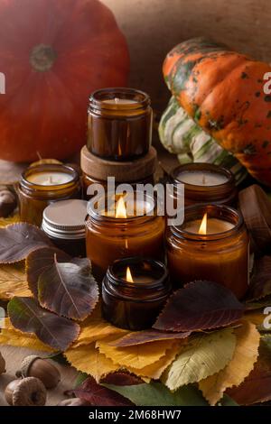 Soy candles burn in glass jars. Tree leaves, pumpkin. Comfort at home. Candle in a brown jar. Scent and light. Scented handmade candle. Aroma therapy. Autumn mood. Cozy home decor in fall. Stock Photo