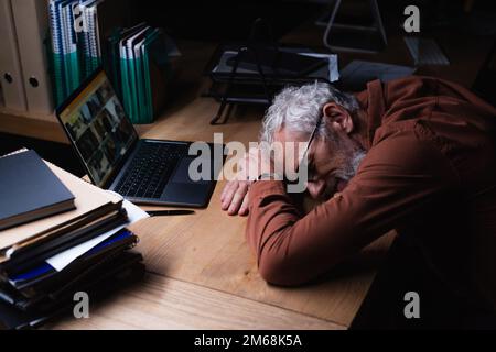 tired grey haired businessman sleeping near laptop and stack of documents in dark office,stock image Stock Photo