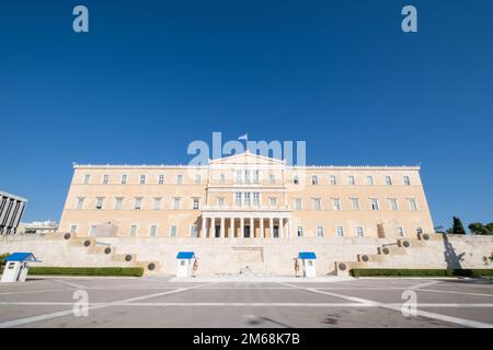 Hellenic Parliament, Athens, Greece, photographed on a bright sunny day with deep blue sky above. A Greek flag flutters on the top, and soldiers of th Stock Photo