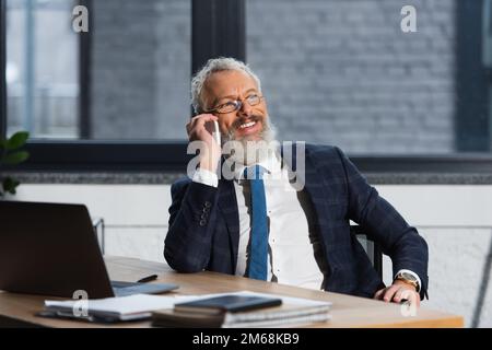 Positive bearded businessman in eyeglasses talking on smartphone in office,stock image Stock Photo
