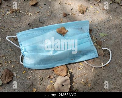 Used disposable medical Blue face mask discarded on the ground of a city road lane. Environmental pollution and waste during the Covid-19 Stock Photo