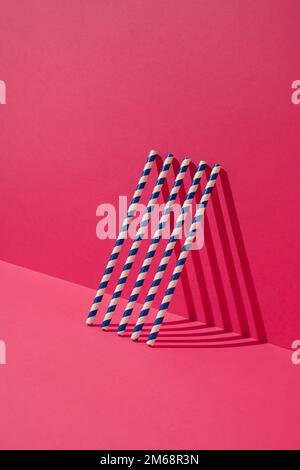Blue striped paper straws leaning on magenta wall. Minimal concept. Stock Photo