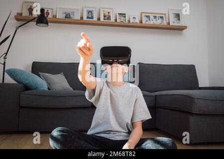 Thrilled boy experiencing the virtual world by using a virtual reality headset looking around and pointing finger Stock Photo
