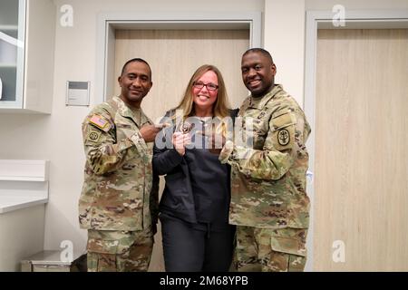 U.S. Army Medical Command Command Sgt. Maj. Diamond D. Hough, left, and Lt. Gen. R. Scott Dingle, right, surgeon general of the Army and MEDCOM commanding general, award Jodie Canez, animal care technician, a coin April 20, 2022 at Chièvres Veterinary Clinic at Chièvres Air Base, Belgium. Stock Photo