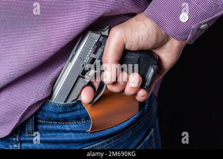 Man In a shirt with pistol on his back. Person holds firearm for attack or defense. Criminal with hand gun Stock Photo