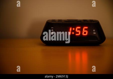 Digital radio alarm clock sitting on a table in a bedroom at night. Dim lighting with shallow depth of field. No logo or branding. Stock Photo