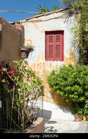 Red shuttered window on a weathered wall of a house in Anafiotika, Athens, Greece, with plants in the foreground. Stock Photo