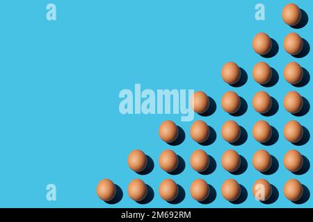 A pattern of brown chicken eggs that lie diagonally on the lower right half of the blue background. Flat lay, copy space. Stock Photo
