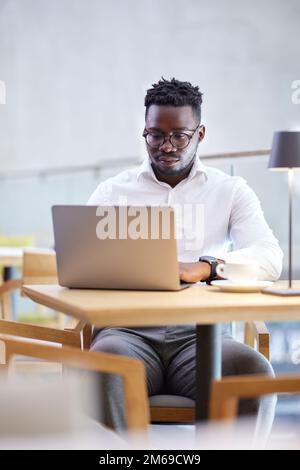 A busy African casual businessman sits in a cafeteria and typing on the laptop. Stock Photo