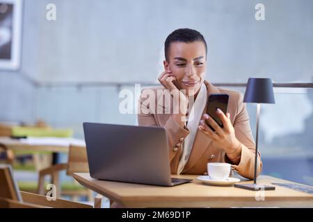 Portrait of a businesswoman casually dressed looking at the phone while sitting in a coffee shop and working. Stock Photo