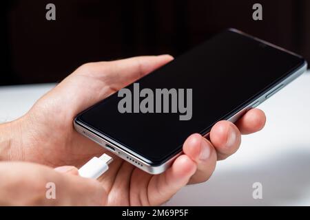 Man hands plugging a charger in a smart phone. Man using smartphone with powerbank. Man charging battery on mobile phone at home Stock Photo