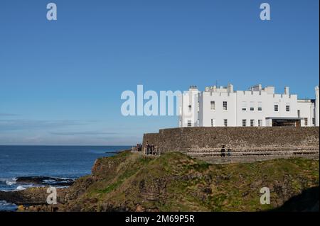 The grand, historic Dominican College building perched dramatically on a clifftop overlooking the sea in Portstewart, with a bright sky overhead.