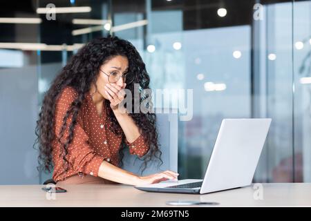 Businesswoman has severe nausea, latin american woman at work sick, working sitting at table with laptop inside office. Stock Photo