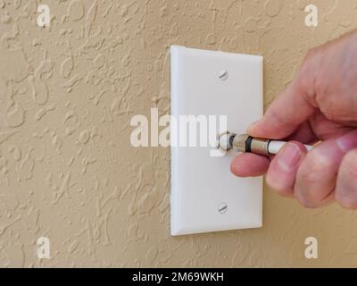 Male electrician connecting coax cable antenna wire to wall outlet. Coaxial connection for TV and high speed broadband internet. Stock Photo