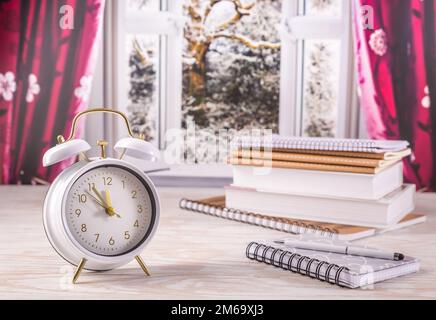 Winter semester, time management concept. Alarm clock with book, notenooks with open window in background Stock Photo