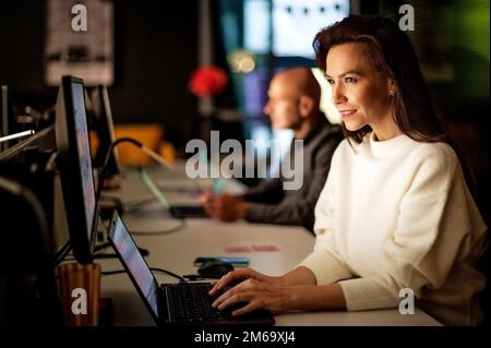 Group of casual business peoples sitting at table with computers and analyzing business information while working in office in late evening. Teamwork. Stock Photo