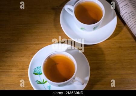 Two cups of tea with folded news paper on a wooden table. Morning light. Stock Photo