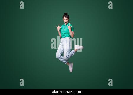 Full body photo of crazy funky woman jump up in air making horned signs screaming isolated on green color background Stock Photo