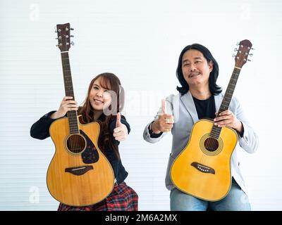 Portrait of Asian duo artists with an acoustic guitar sitting on a white background and show the gesture of thumps up for music, artist, musician conc Stock Photo